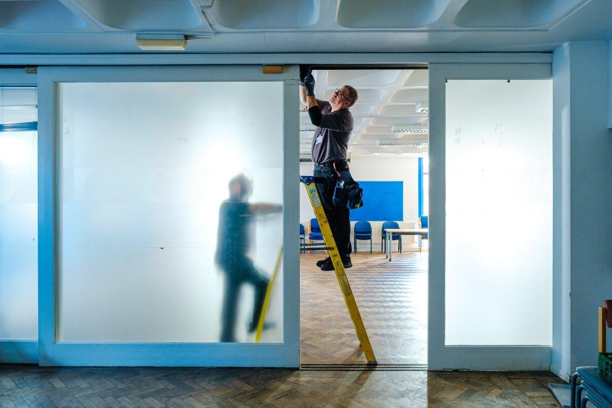 Mitie maintenance engineer up a ladder fixing a door at Sussex University